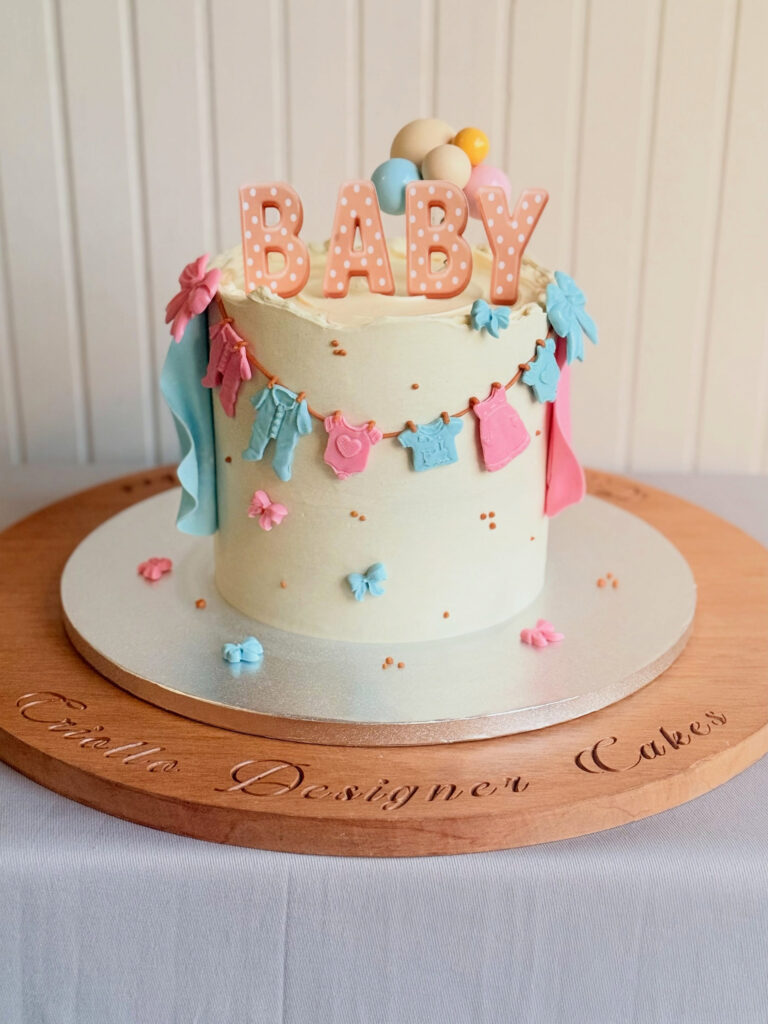 Neutral buttercream gender reveal cake with pink and blue baby clothes, bows and BABY topper in Dunedin